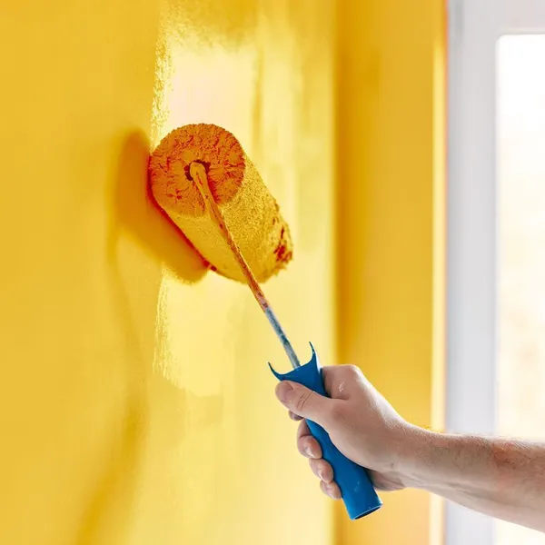 Una persona utilizza un rullo da pittura per applicare la vernice su una parete in un ambiente di ristrutturazione.