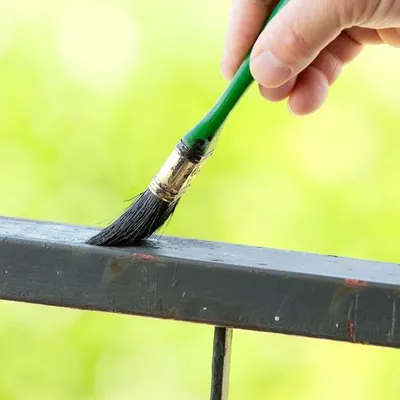 Una persona che dipinge una ringhiera con un pennello, concentrata sull'applicazione di una mano di vernice fresca.